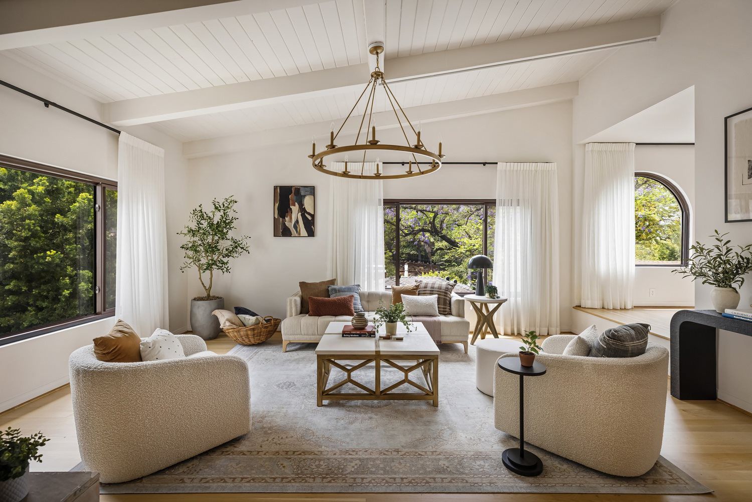 Elegant living room with vaulted beam ceilings, floor-to-ceiling stone fireplace, hardwood floors, large picture windows, designer furnishings, and abundant natural light.