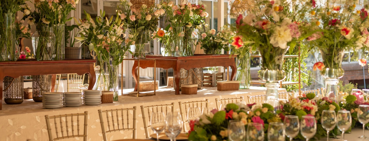 Indoor micro wedding reception with natural wood tables, simple place settings, lush greenery centerpieces, and a relaxed lounge area — holiday proposal planning by Weddings & Events by K’Mich
