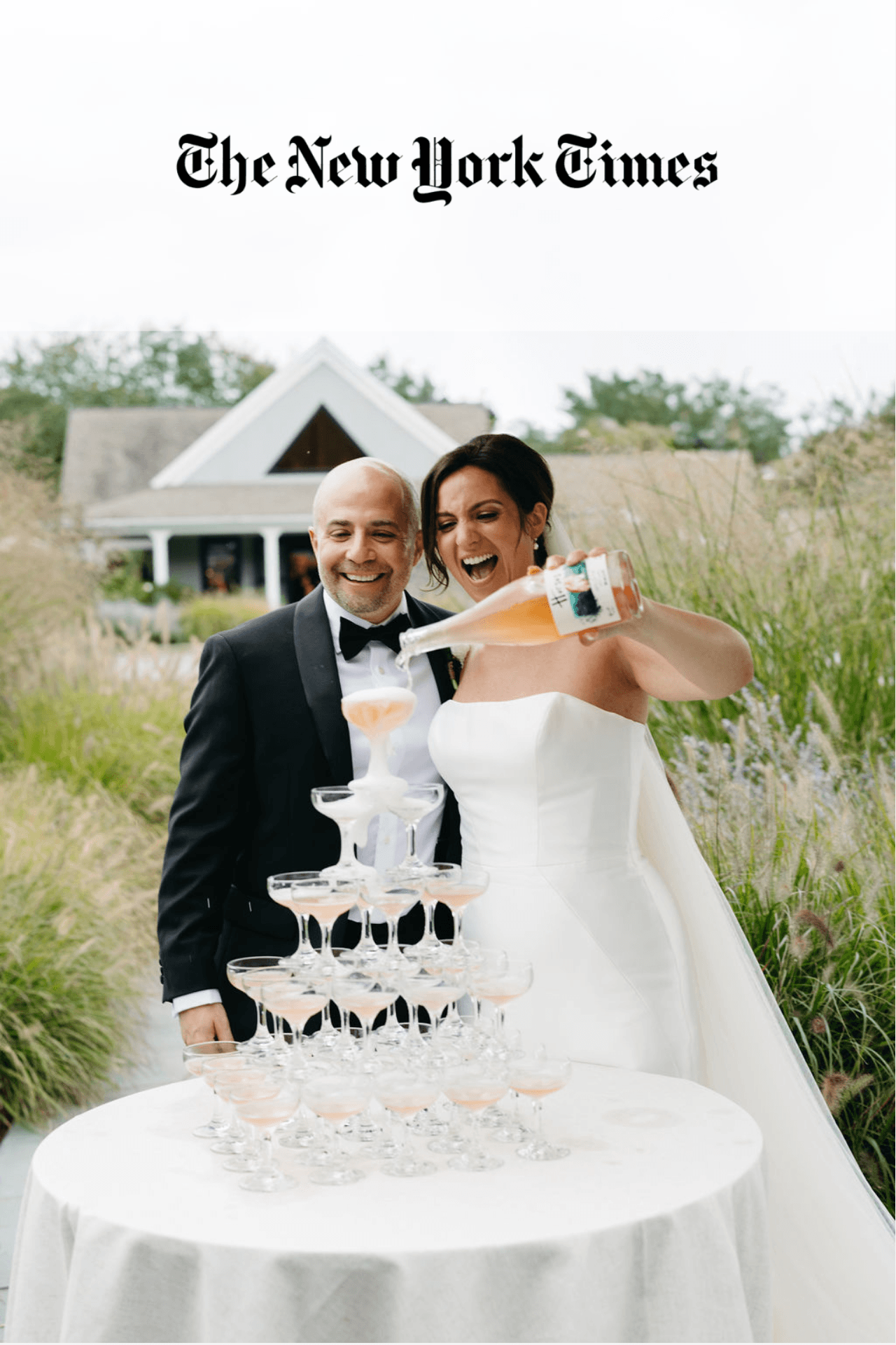Bride and groom smiling in an outdoor setting with the bride pouring champagne into a tower of champagne glasses.