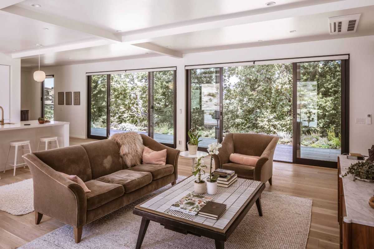 All Weather Series 8150 aluminum sliding patio doors with four glass panels connect a modern living room to the backyard.