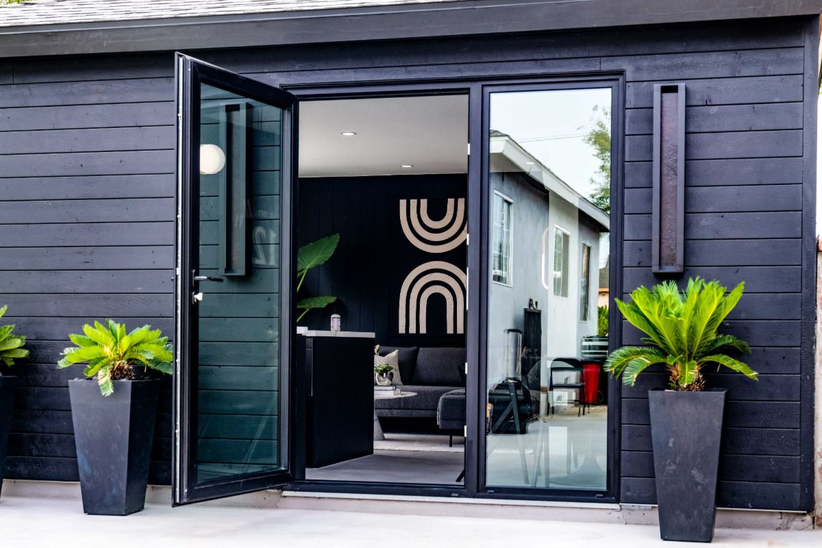 All Weather Series 7000 aluminum swing door with a black frame opens to a contemporary home's outdoor patio.
