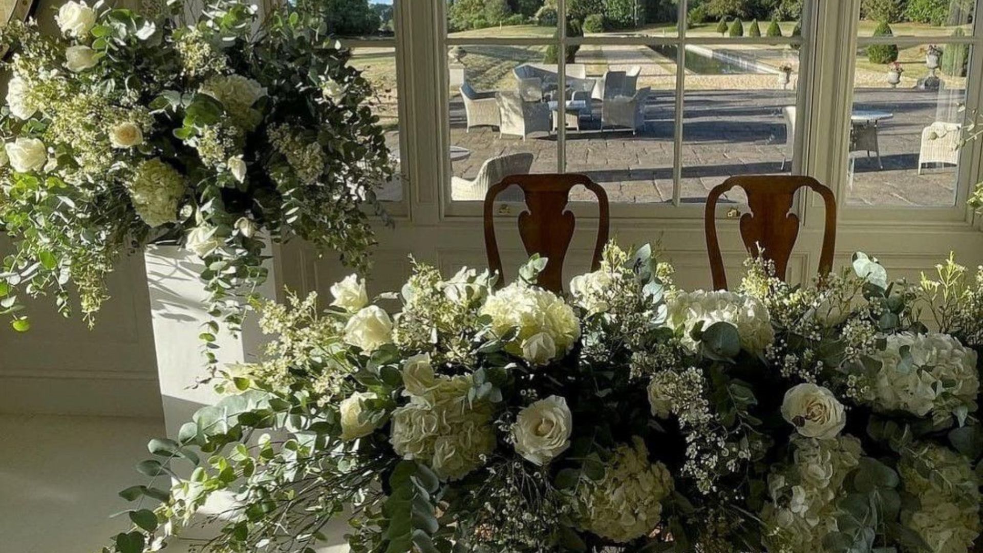 Elegant wedding head table with white roses, hydrangeas, eucalyptus greenery, and natural light styling by Weddings & Events by K’Mich