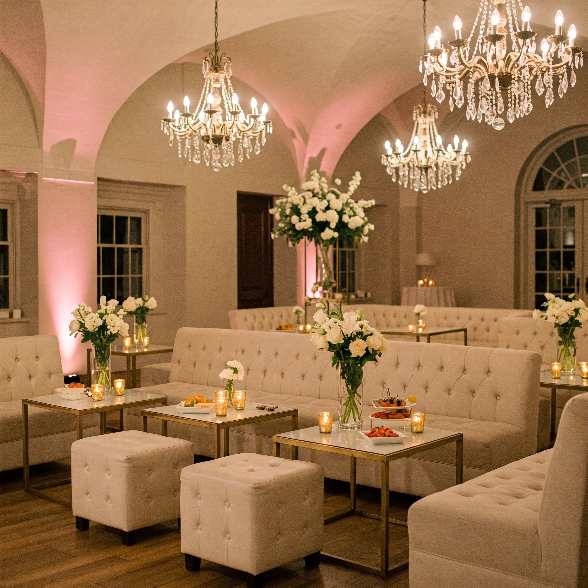 Elegant wedding reception lounge with chandeliers, ivory tufted seating, and white rose floral arrangements designed for wedding reception by Weddings & Events By K'Mich in Philladelphia, PA