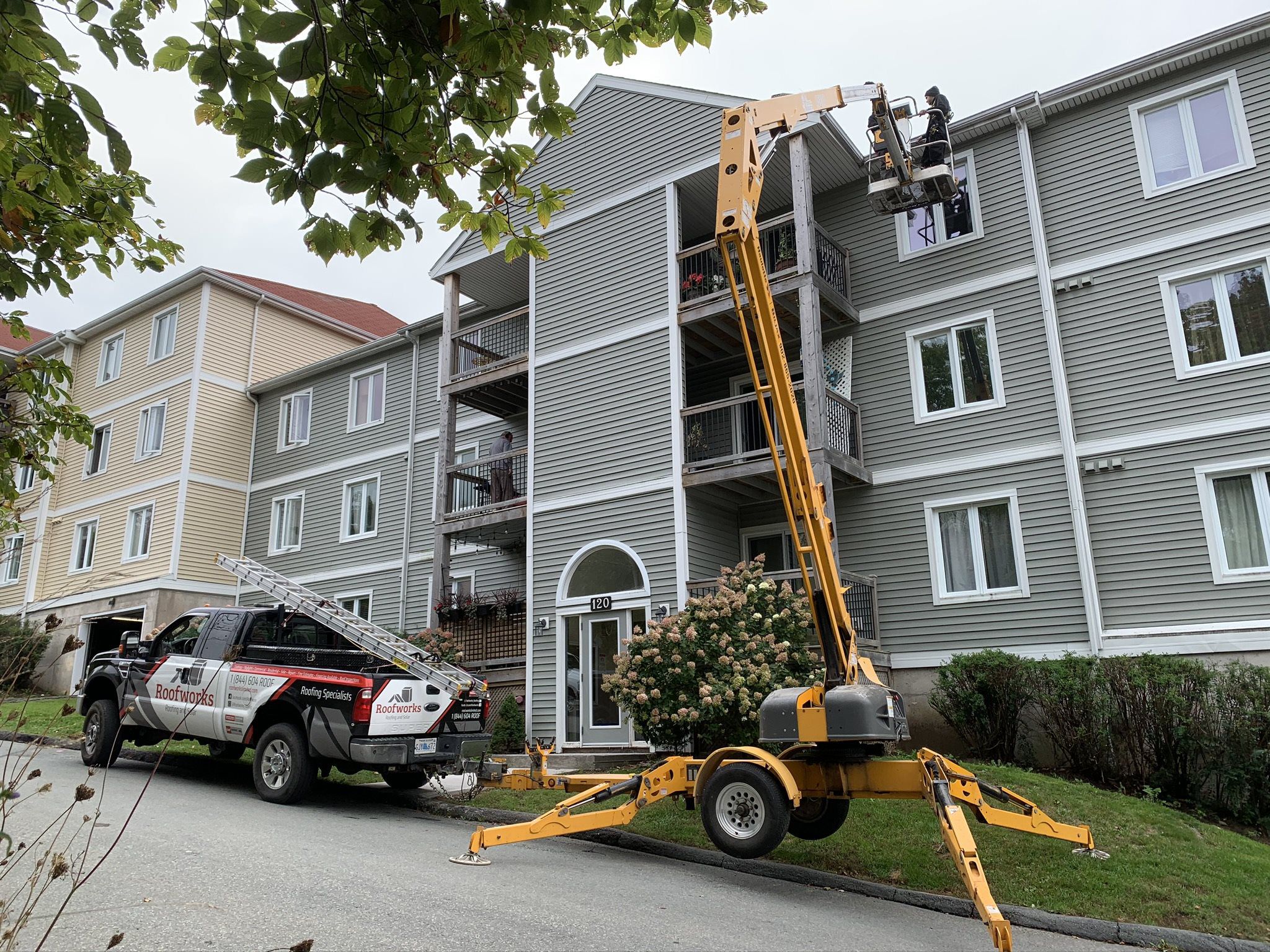 Two men working off of arial equipment to replace roof on large Condominium building