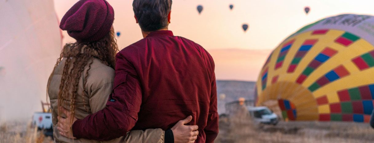 Engaged couple watching sunrise hot air balloons together — romantic adventure moment for engagement gift inspiration by Weddings by K’Mich.