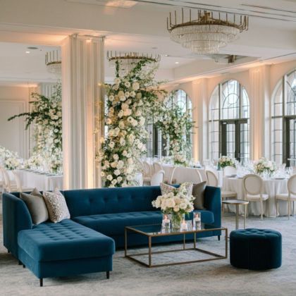 Elegant white wedding ballroom with blue velvet lounge seating, crystal chandeliers, and white rose floral arches in upscale Philadelphia venue designed by Weddings & Events by K'mich