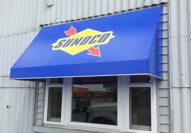 A storefront awning displaying a brand logo in vibrant colors, mounted above the entrance of a retail store. This commercial awning and canopy design enhances brand visibility while providing shade. The awning material is durable, suitable for both c