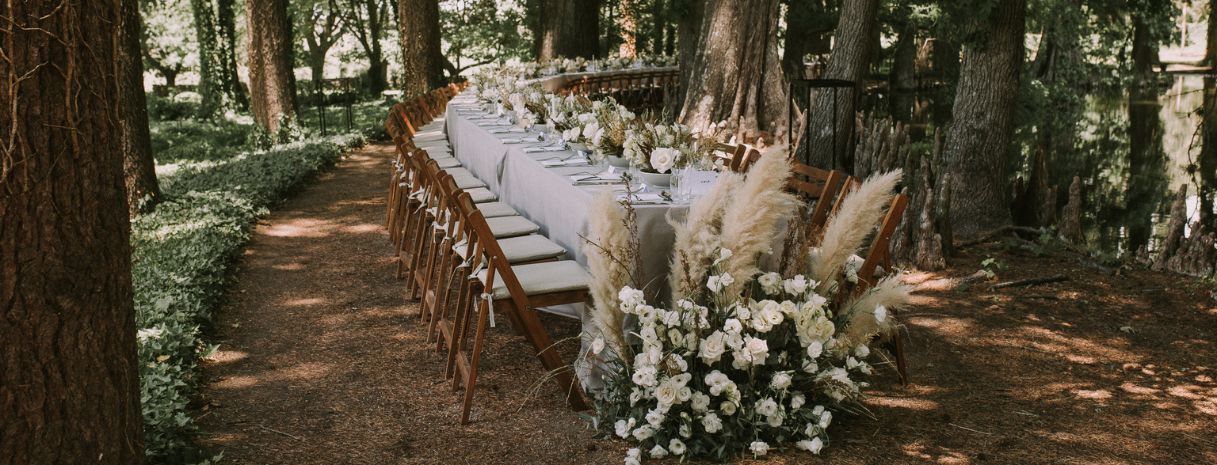 Outdoor Philadelphia wedding reception with a long farmhouse table, white linens, wooden chairs, and lush neutral florals. Ideas styled for a $30K wedding budget hosting 150 guests by Weddings & Events by K’Mich.
