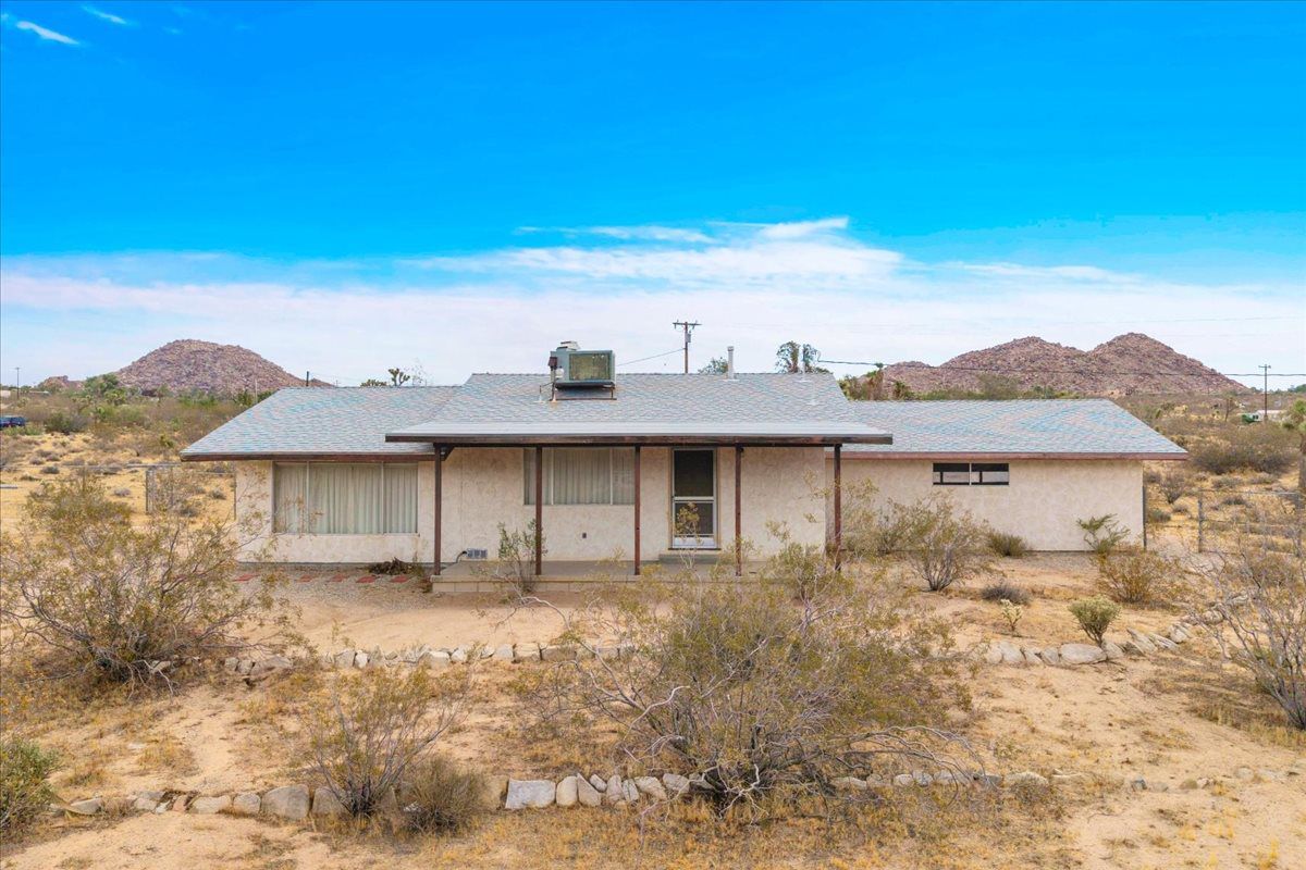 Single-story desert home surrounded by native shrubs and rocky hills under a bright blue sky.