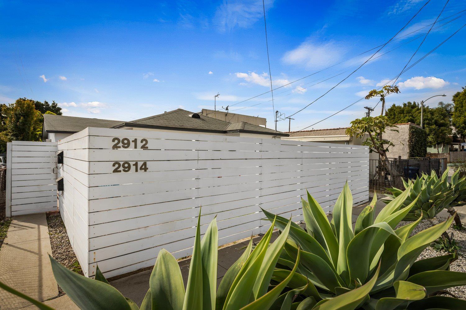 Exterior view of a modern Los Angeles home in the 90026 area part of a duplex featuring a white horizontal privacy fence, visible address numbers, and drought-tolerant landscaping.