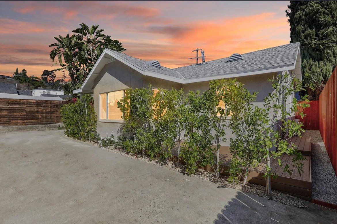 Modern single-family home in Los Angeles CA 90041 featuring a gray exterior, private driveway, greenery, and sunset sky.