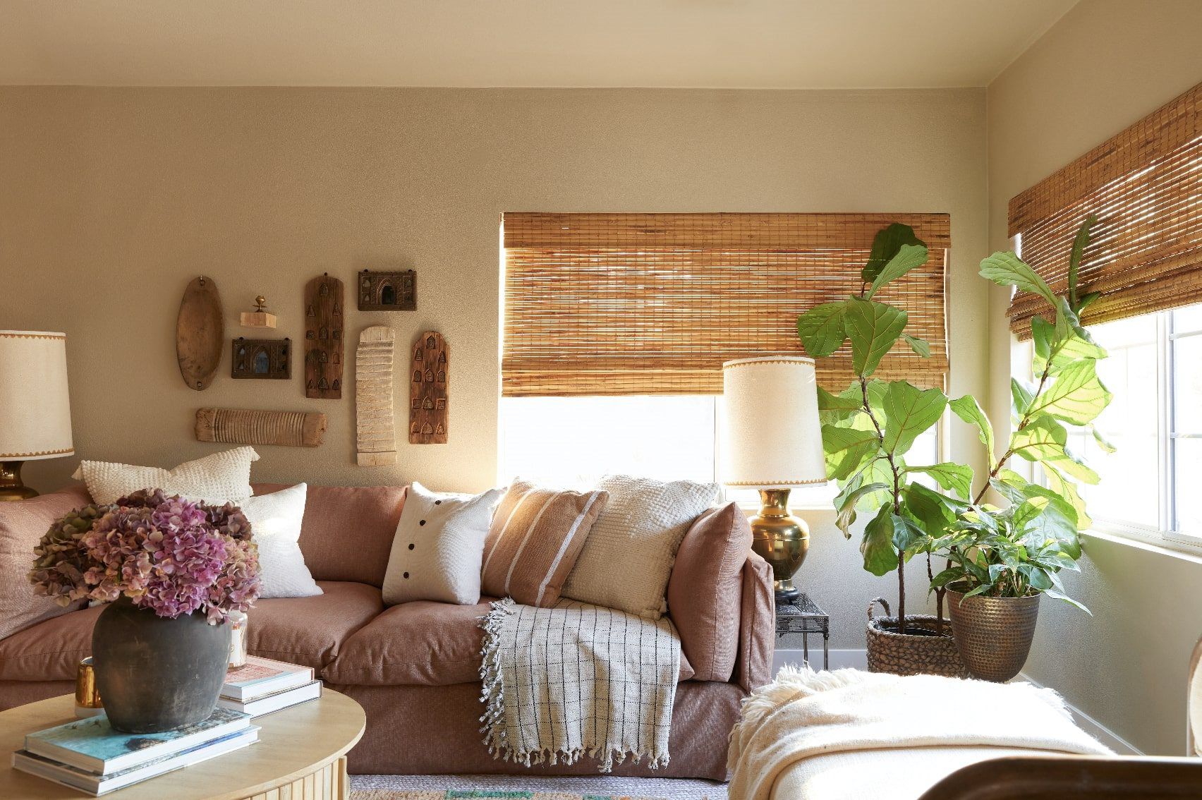 Warm living room with tan sofa, bamboo shades, wall art, and a fiddle-leaf fig plant.