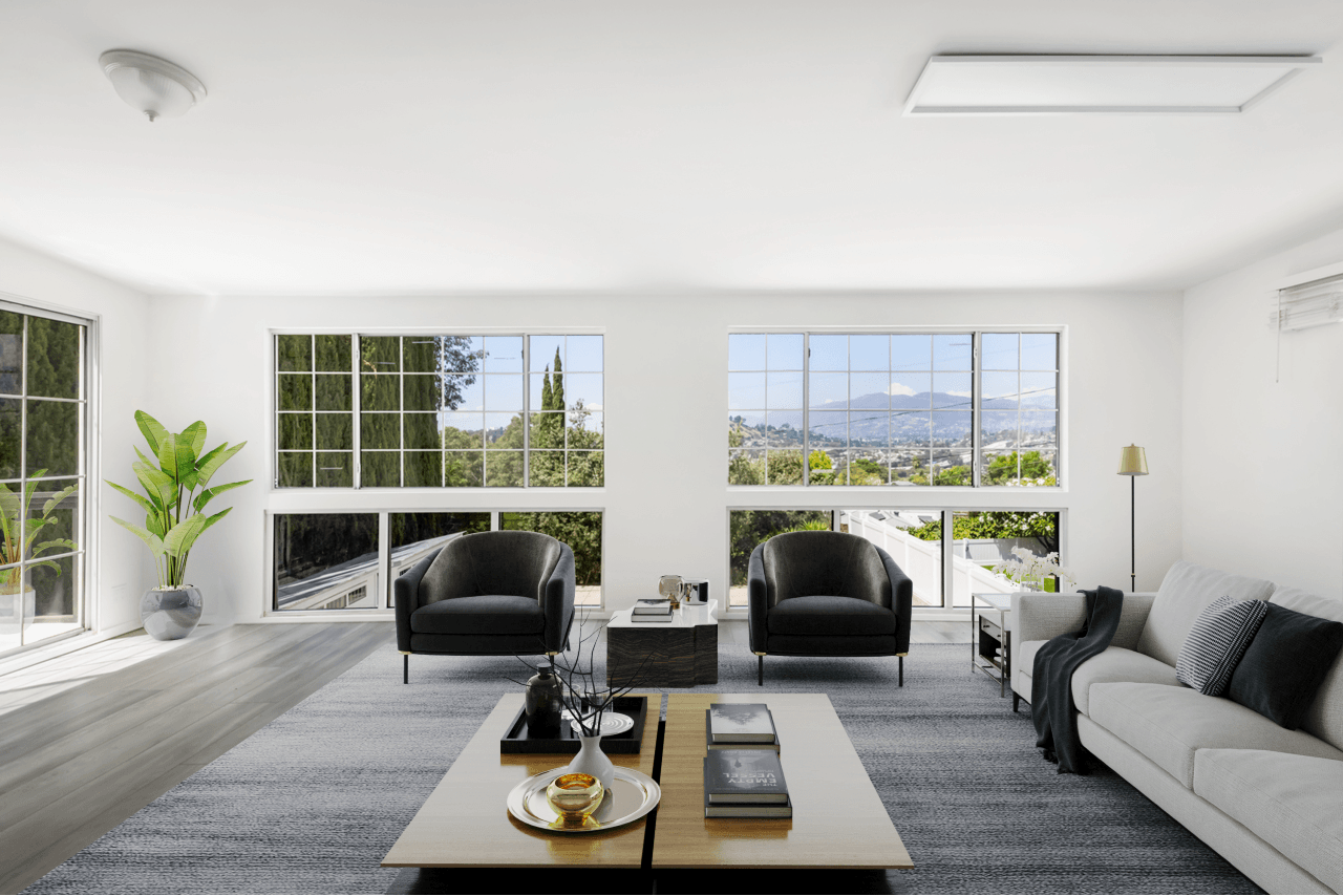 Spacious modern living room with large windows, gray sofa, two black armchairs, coffee table, and scenic mountain views.